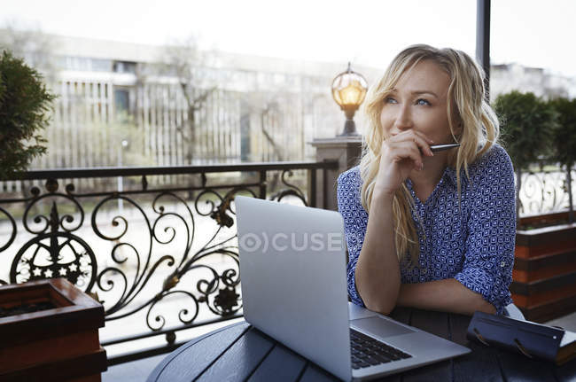 Pensante blogger donna che lavora nel caffè, utilizzando computer portatile e tenendo la penna — Foto stock