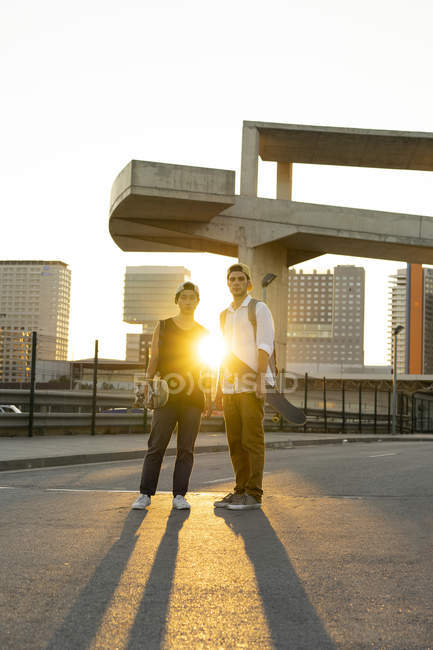 Portrait of two young men with skateboards in the city at sunset — Stock Photo