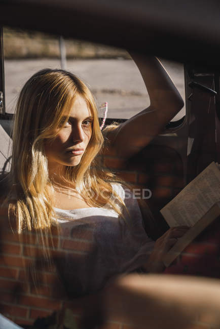 Portrait de jeune femme assise dans une voiture, livre de lecture — Photo de stock