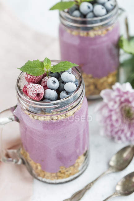 Two glasses of yoghurt with peanut granola, aronia powder and topping of hazelnuts and frosted berries — Stock Photo