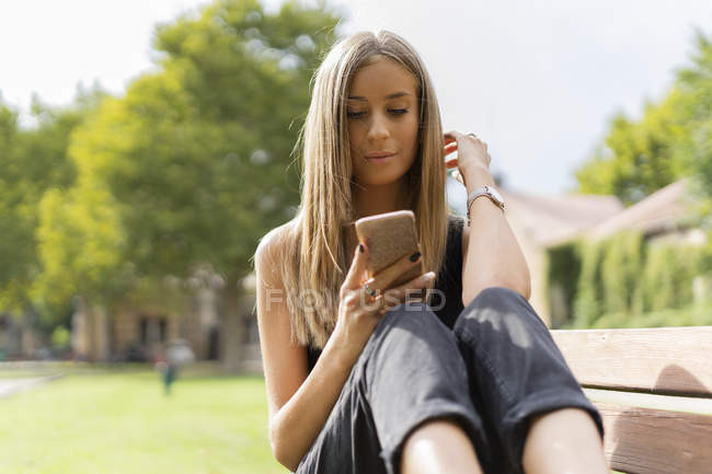 Расслабленная девушка-подросток сидит на скамейке и пользуется мобильным телефоном — стоковое фото