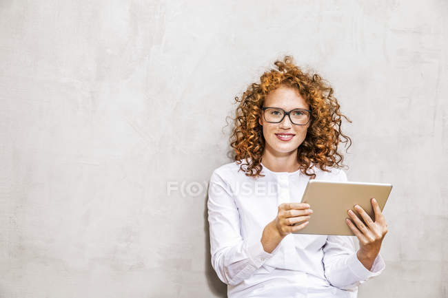 Портрет редчолі молодої жінки з планшетом сидить перед сірої стіною — стокове фото