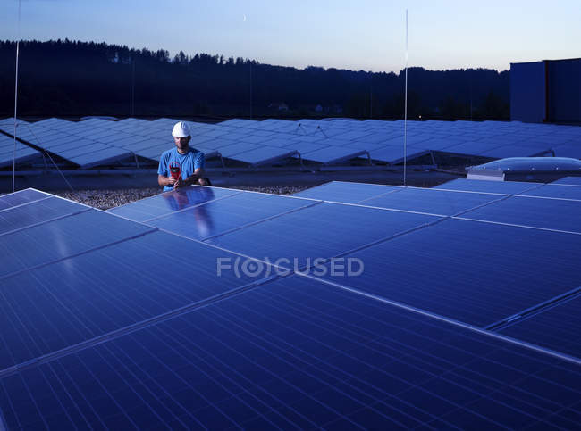 Trabajador con dispositivo de medición de verificación de la planta solar por la noche - foto de stock