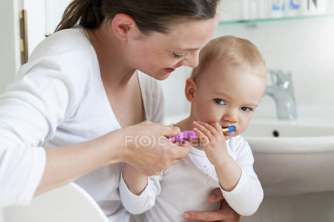 Mother brushing baby's teeth in bathroom — Stock Photo
