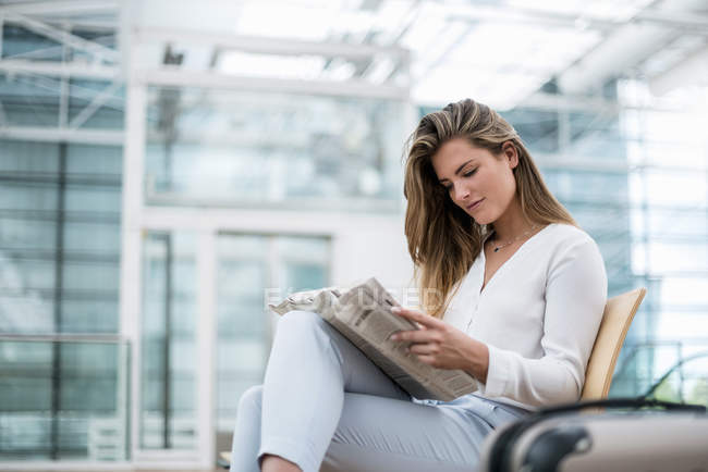 Young businesswoman sitting outdoors with suitcase reading newspaper — Stock Photo