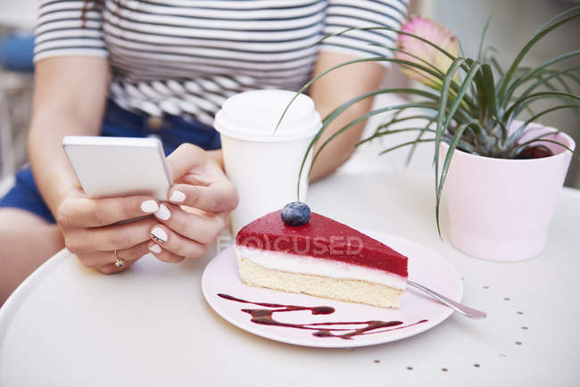 Primer plano de la mujer usando el teléfono celular y comiendo pastel en un  café — tarta, Mensaje - Stock Photo | #268347312