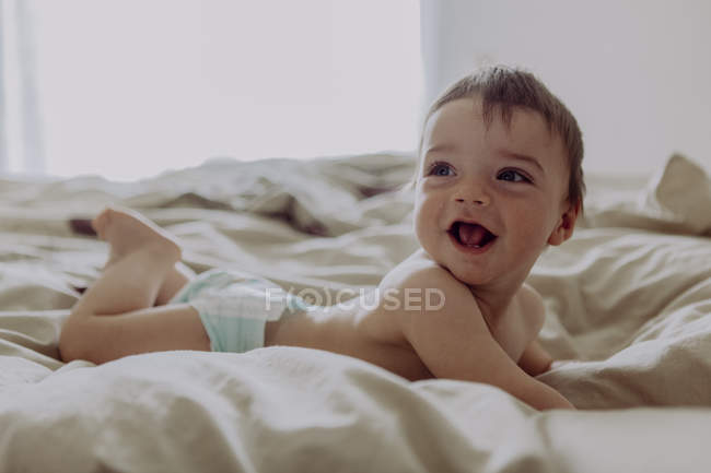 Щаслива дитина, лежить на ліжку, сміється — стокове фото