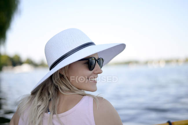 Smiling young woman wearing sunglasses and white summer hat al lake — Stock Photo