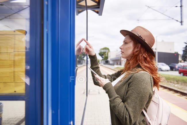 Redheaded young woman looking at timetable on platform — Stock Photo
