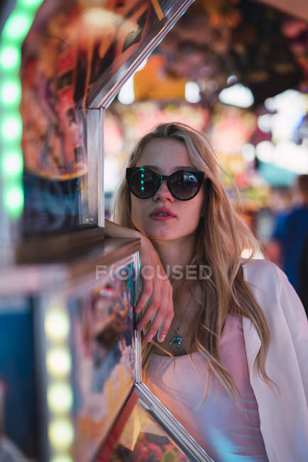 Portrait of young woman wearing sunglasses and posing in amusement park — Stock Photo