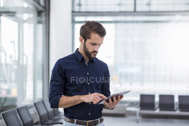 Jeune homme d'affaires debout dans la salle d'attente en utilisant tablette — Photo de stock
