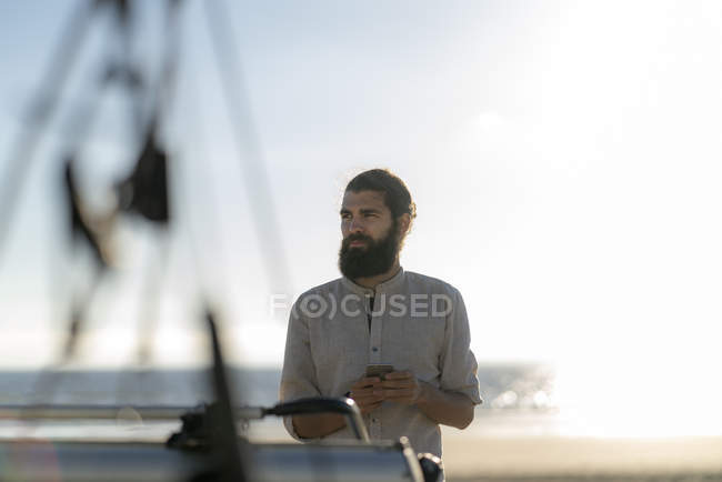 Молодой человек использует смартфон на пляже — стоковое фото