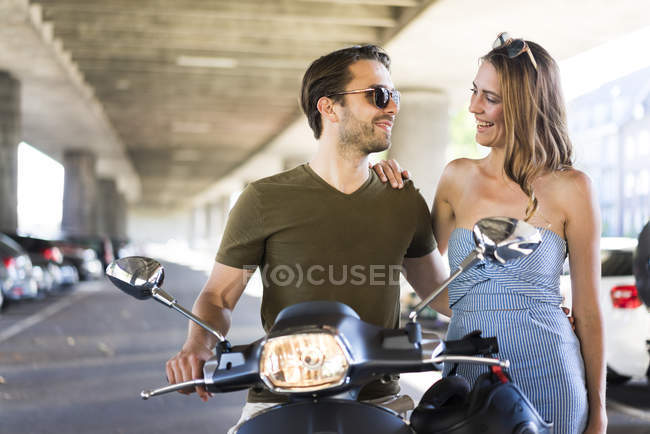Casal com scooter motor sorrindo um para o outro em underpass — Fotografia de Stock