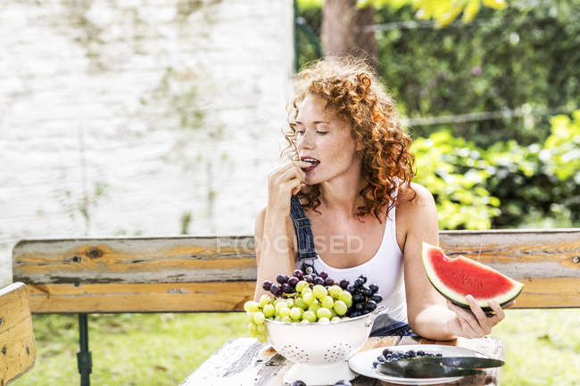 Redheaded young woman eating grapes at rustic table in summer — Stock Photo