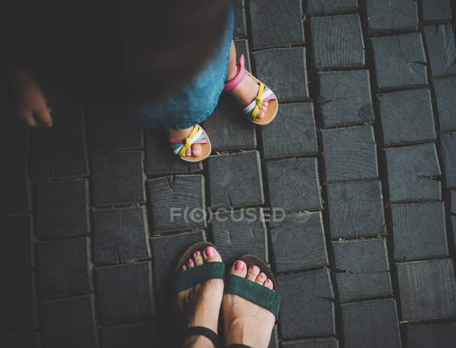 Pies de niña y su madre de pie sobre pavimento de madera, vista superior - foto de stock