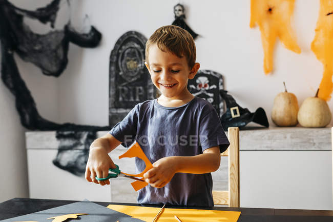 Smiling little boy cutting out for Halloween decoration at home scissors — Stock Photo