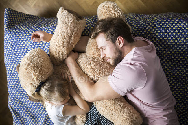 Батько з дочкою дрімають, обіймаючись з Тедді ведмедем. — стокове фото
