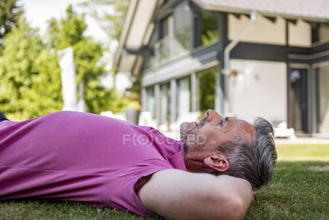 Uomo maturo sdraiato nel giardino della sua casa — Foto stock