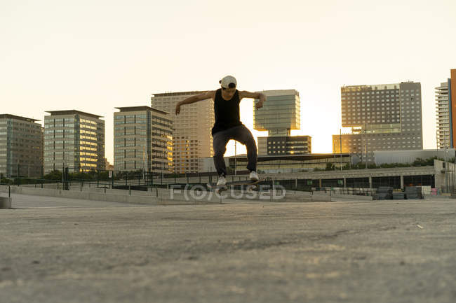 Young man doing a skateboard trick in the city at sunset — Stock Photo
