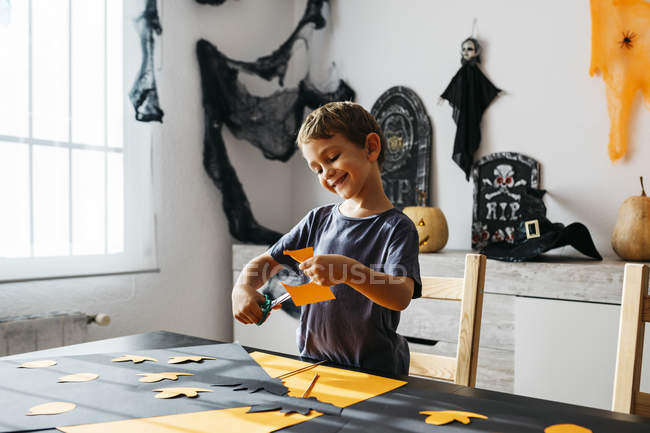 Sonriente niño recortando para la decoración de Halloween con tijeras - foto de stock