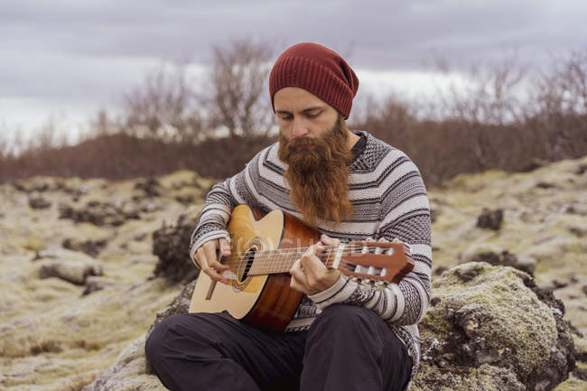 Homem sentado no deserto, tocando guitarra — Fotografia de Stock