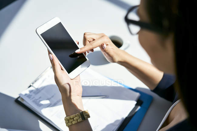Primer plano de la mujer de negocios utilizando el teléfono celular en el escritorio en la oficina - foto de stock