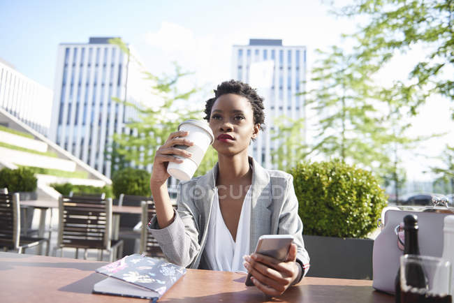 Retrato de empresária com telefone celular bebendo café no café da calçada — Fotografia de Stock