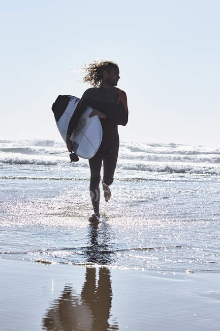 Впевнений чоловік біжить у воді з дошкою для серфінгу — стокове фото
