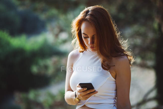 Redheaded woman using cell phone outdoors — Stock Photo