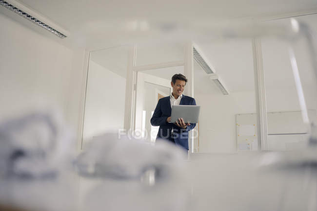 Empresário de pé no escritório, usando laptop — Fotografia de Stock