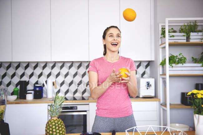 Portrait of young woman juggling with oranges in kitchen — Stock Photo