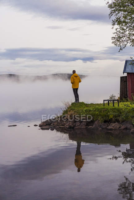 Самотній чоловік стоїть на озері, дивлячись на туман і воду — стокове фото