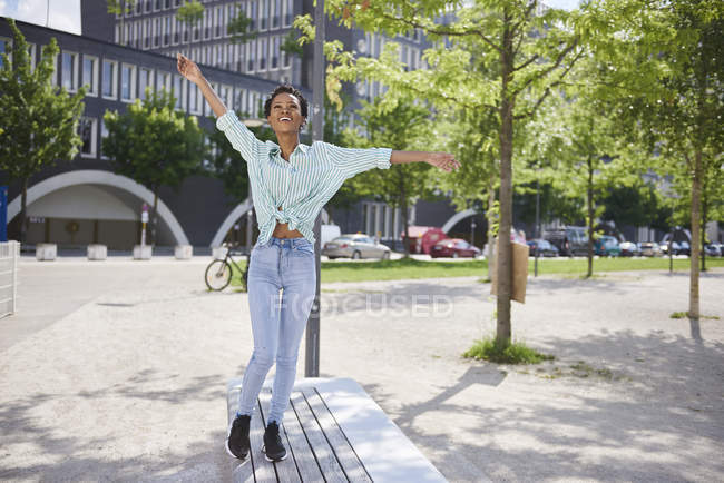 Счастливая молодая женщина балансирует на скамейке — стоковое фото
