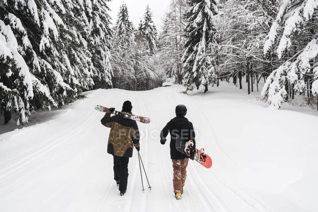 Италия, Модена, Чимоне, вид сзади на пару с лыжниками и сноубордистами, гуляющими по зимнему лесу — стоковое фото