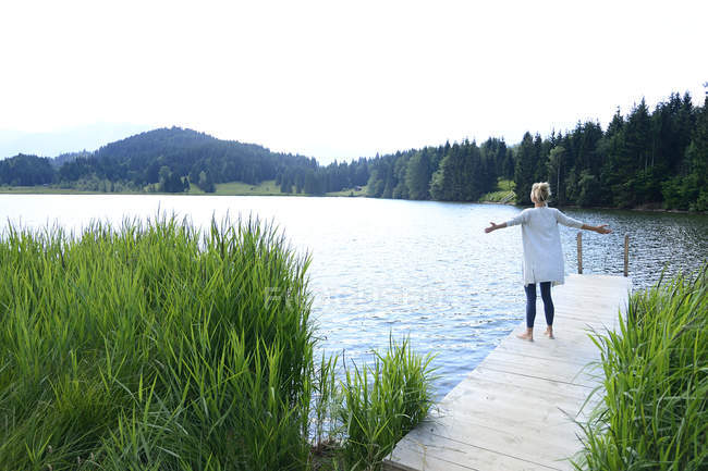 Alemanha, Mittenwald, vista traseira da mulher de pé com os braços estendidos no molhe no lago — Fotografia de Stock