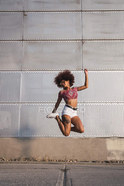 Giovane donna alla moda che salta in aria contro muro di costruzione — Foto stock