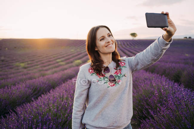 Francia, Valensole, ritratto di una donna sorridente che fa selfie davanti al campo di lavanda al tramonto — Foto stock
