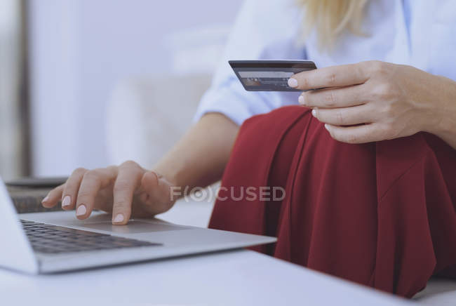 Частковий вид на жінку за столом, що тримає кредитну картку і ноутбук. — стокове фото