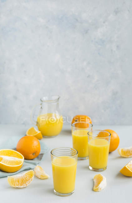Vasos de zumo de naranja recién exprimido y naranjas - foto de stock