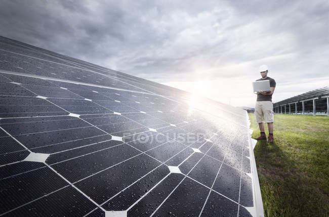 Engineer with laptop checking solar plant at evening twilight — Stock Photo
