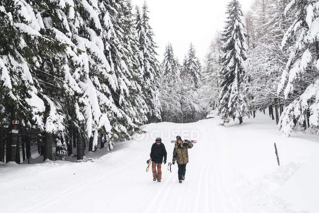Италия, Модена, Чимоне, пара с лыжниками и сноубордистами, гуляющими по зимнему лесу — стоковое фото