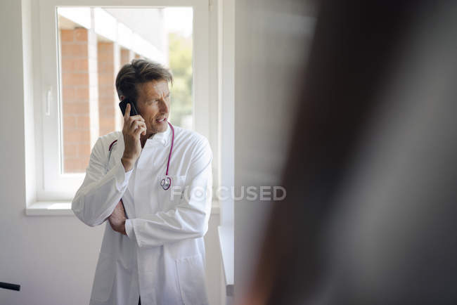 Médico de pie en el hospital, usando smartphone - foto de stock