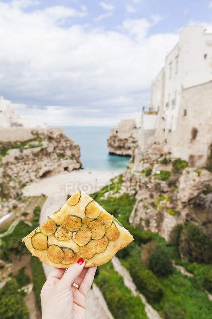 Italy, Puglia, Polognano a Mare, woman's hand holding piece of zucchini focaccia — Stock Photo