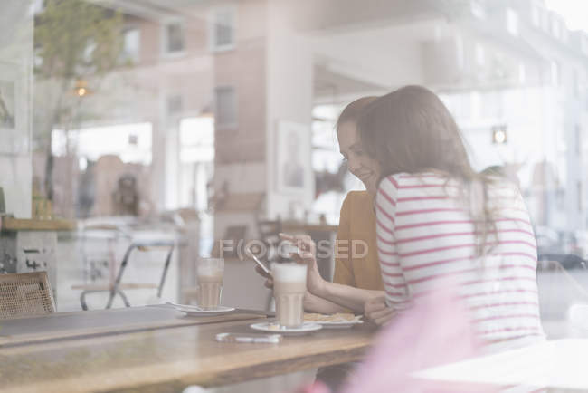 Two girlfriends meeting in a coffee shop, using smartphone — Stock Photo
