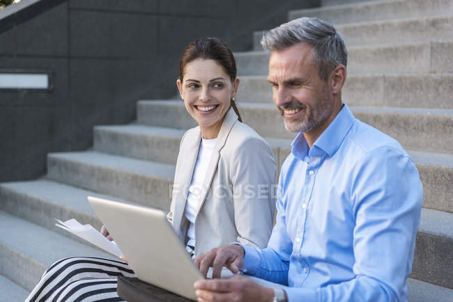 Two business people sitting side by side on stairs working together — Stock Photo
