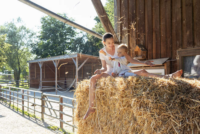Mãe feliz e filha brincando com palha em um celeiro — Fotografia de Stock