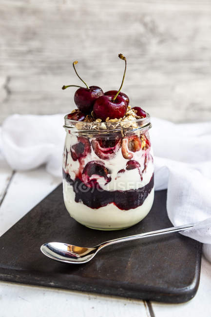 Glass of natural yoghurt with cherries, cherry jam and granola — Stock Photo