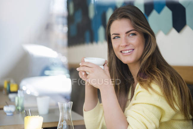 Усміхнена молода жінка в кафе тримає чашку кави — стокове фото