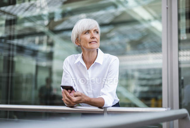 Seniorin lehnt mit Handy an Geländer in der Stadt — Stockfoto