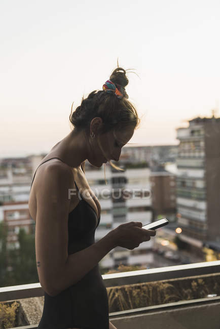 Jeune femme portant une robe noire en utilisant un téléphone portable sur le balcon — Photo de stock